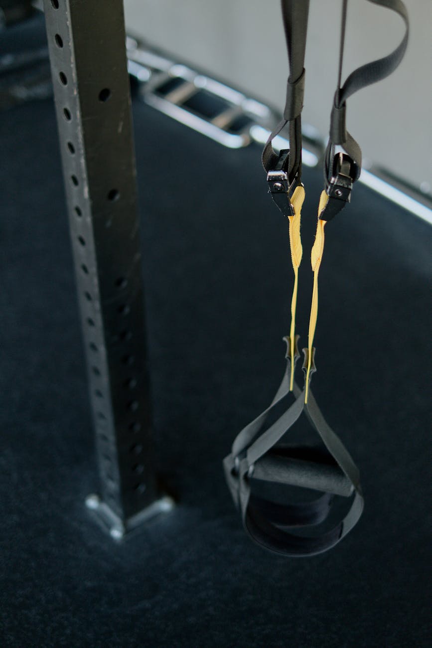 A black resistance band hanging from a metal pole in a gym. The resistance band is attached to the pole with two straps, one ...