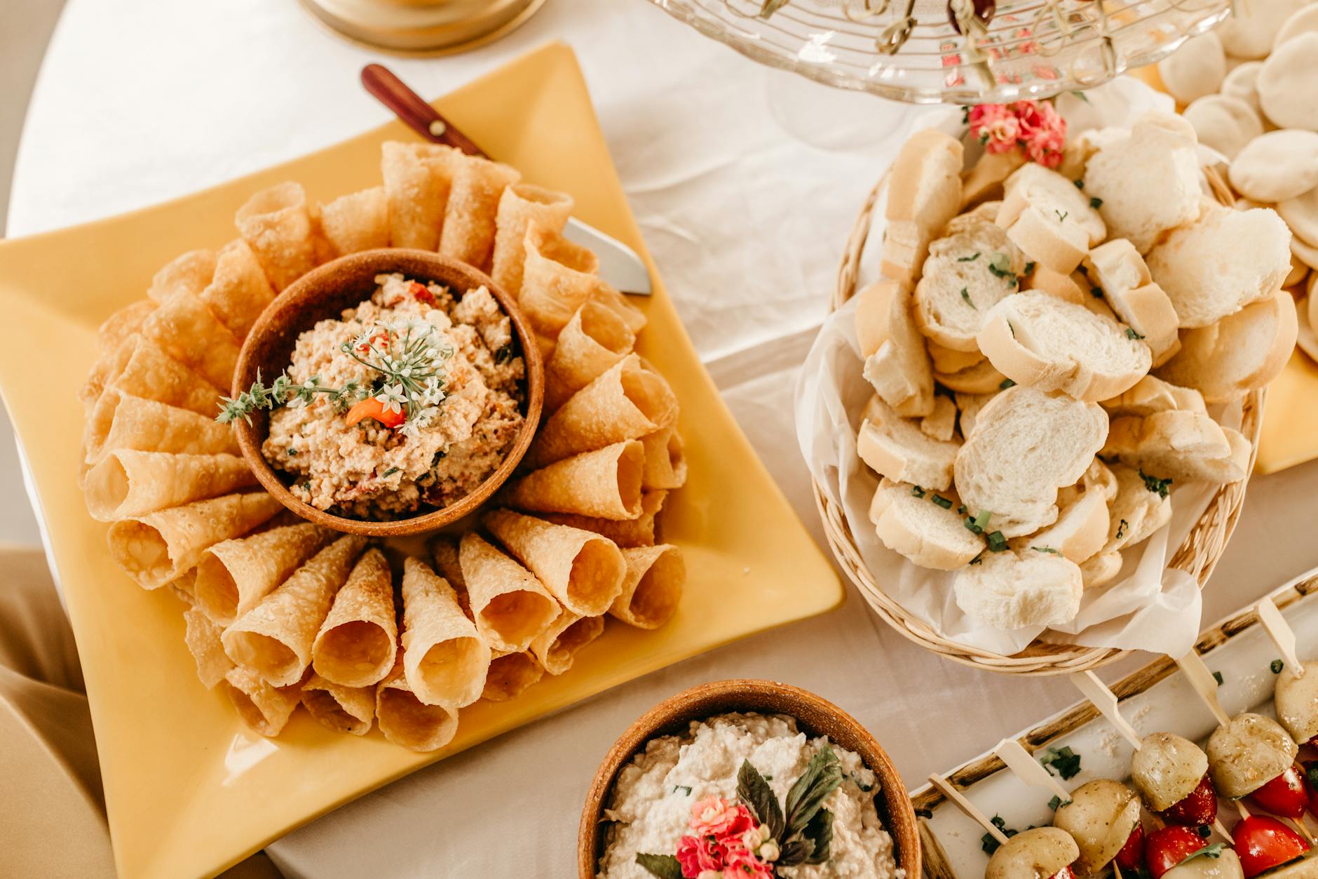 A table with a variety of food items arranged on it. On the left side of the table, there is a yellow rectangular plate with ...