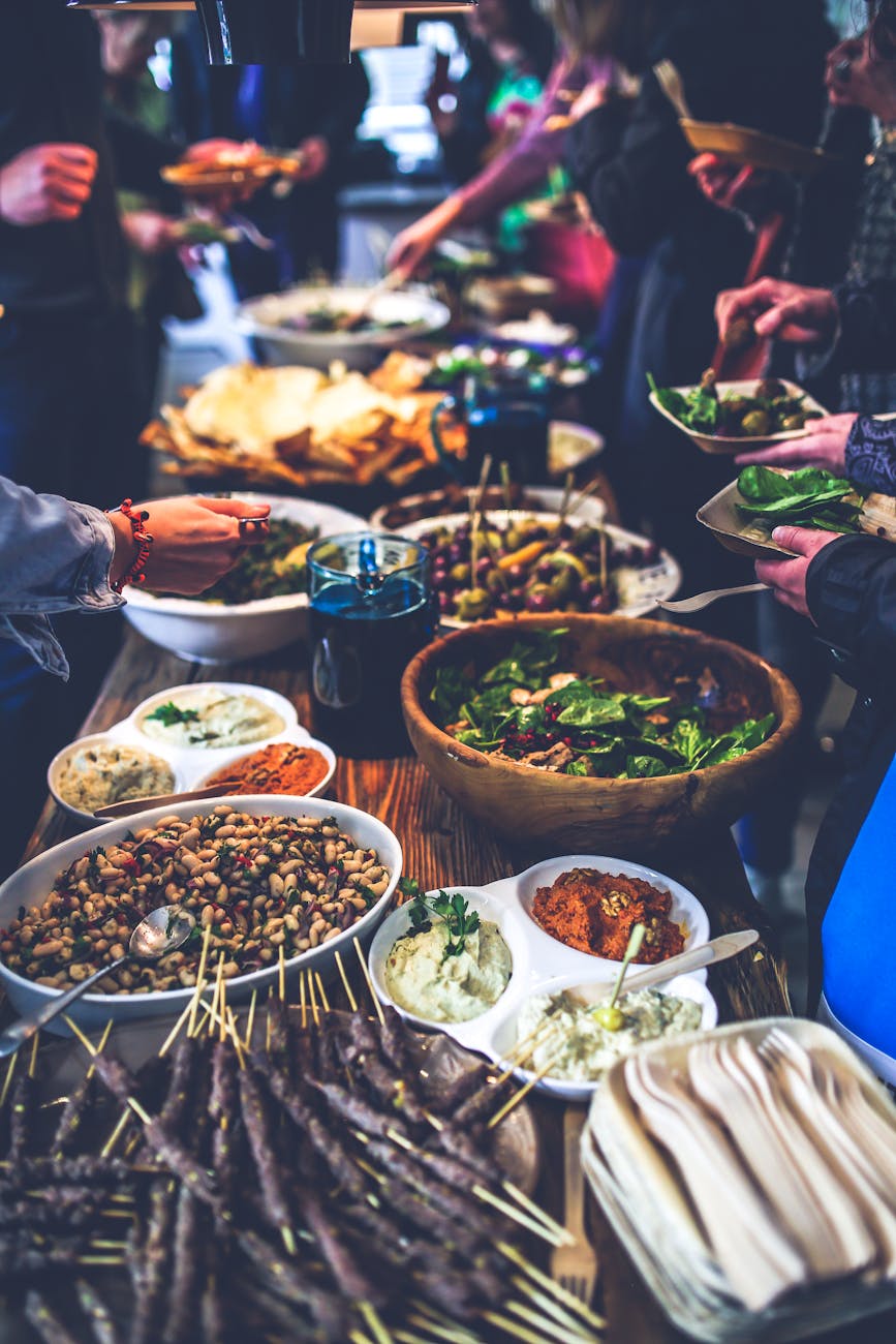A group of people gathered around a long table filled with various types of food. The table is covered with a variety of dish...