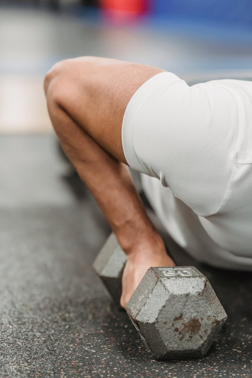 A person's lower body in a gym, holding a dumbbell. The person is wearing white shorts and appears to be in the middle of a w...