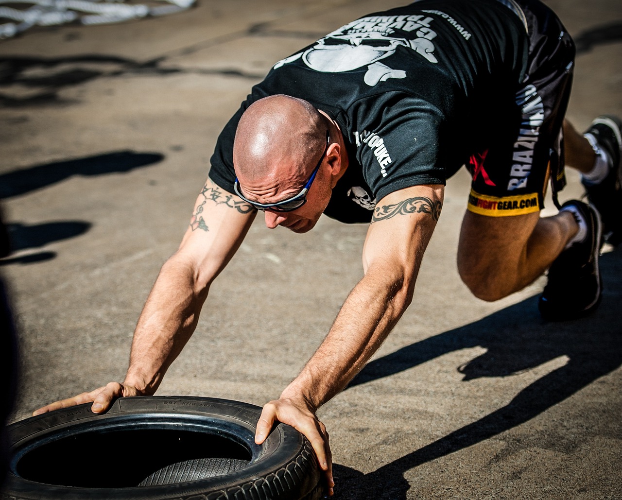 A man in a black t-shirt with a skull and crossbones design on it, bending over a black tire. He is wearing sunglasses and ap...